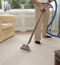 Professional carpet cleaner using a hot-water extraction wand and hose machine in a living room in Birmingham, AL.