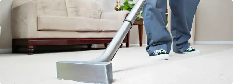 Carpet cleaning technician using a hot-water extraction wand on a light-colored carpet in a living room, Birmingham, AL.