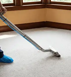 Steam carpet cleaning technician using a hot-water extraction wand on a residential carpet, wearing blue protective shoe covers Birmingham, AL.