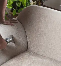 Professional upholstery cleaner deep-cleaning a fabric sofa with a handheld extraction tool and hose Birmingham, AL.