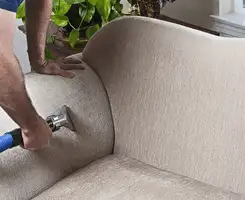 Professional upholstery cleaner deep-cleaning a fabric sofa with a handheld extraction tool and hose in Birmingham, AL.